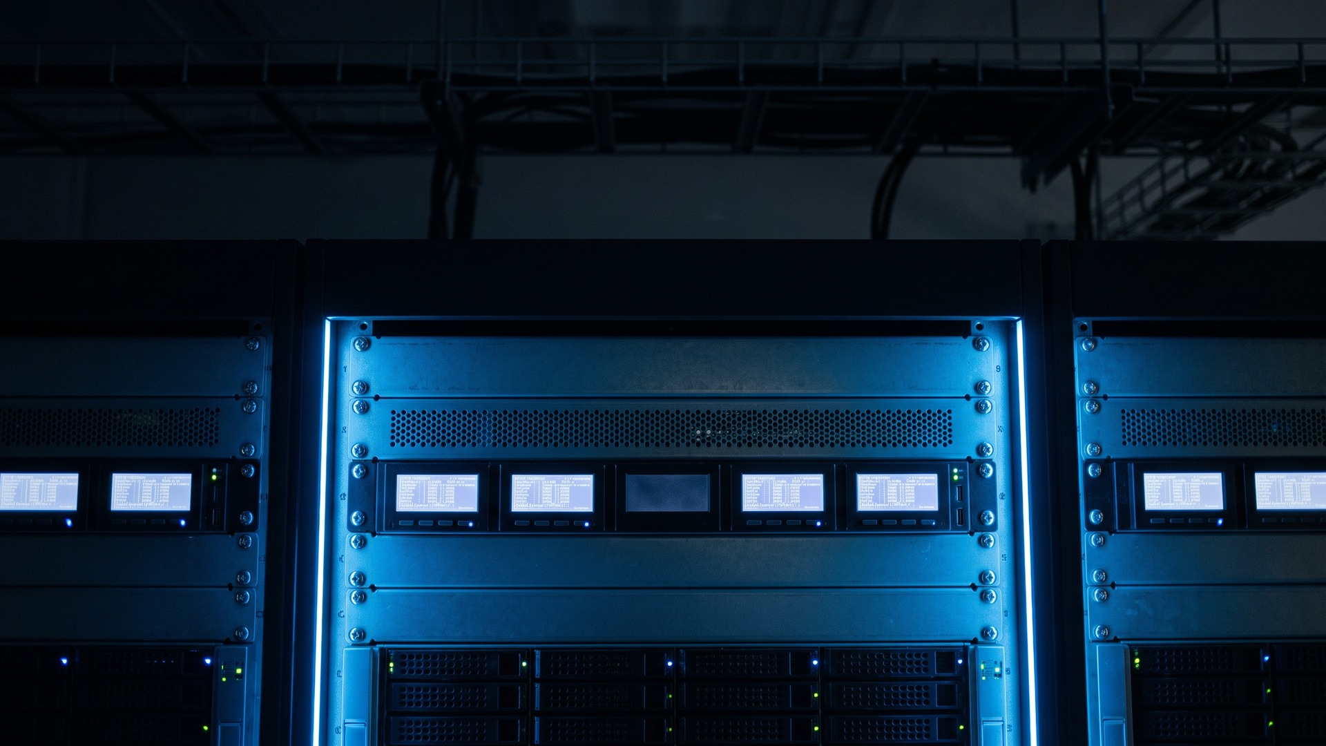 A dark server room with one rack's activity display left blank while neighbouring displays show scrolling entries