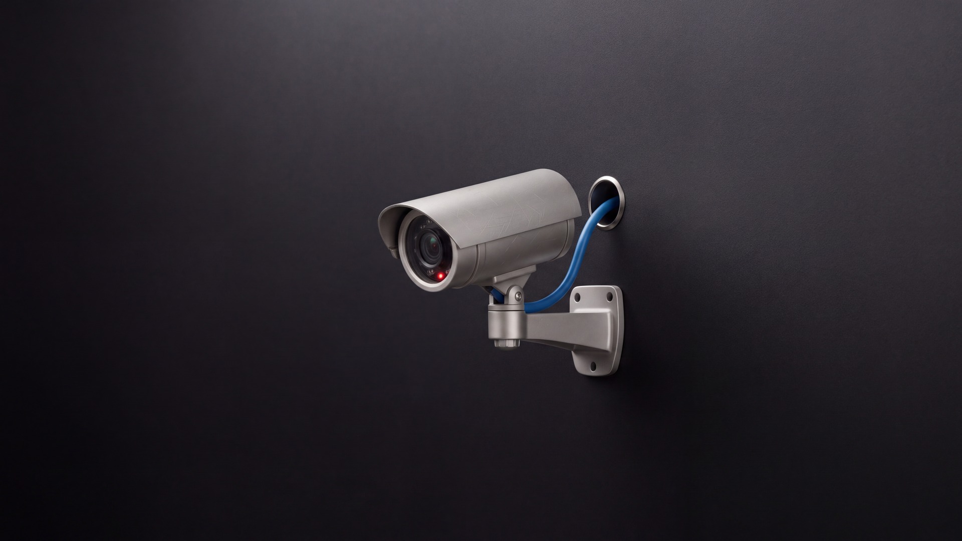 Top 5 Cybersecurity News illustration of a security camera on a black wall with a blue cable passing through a hole in the wall